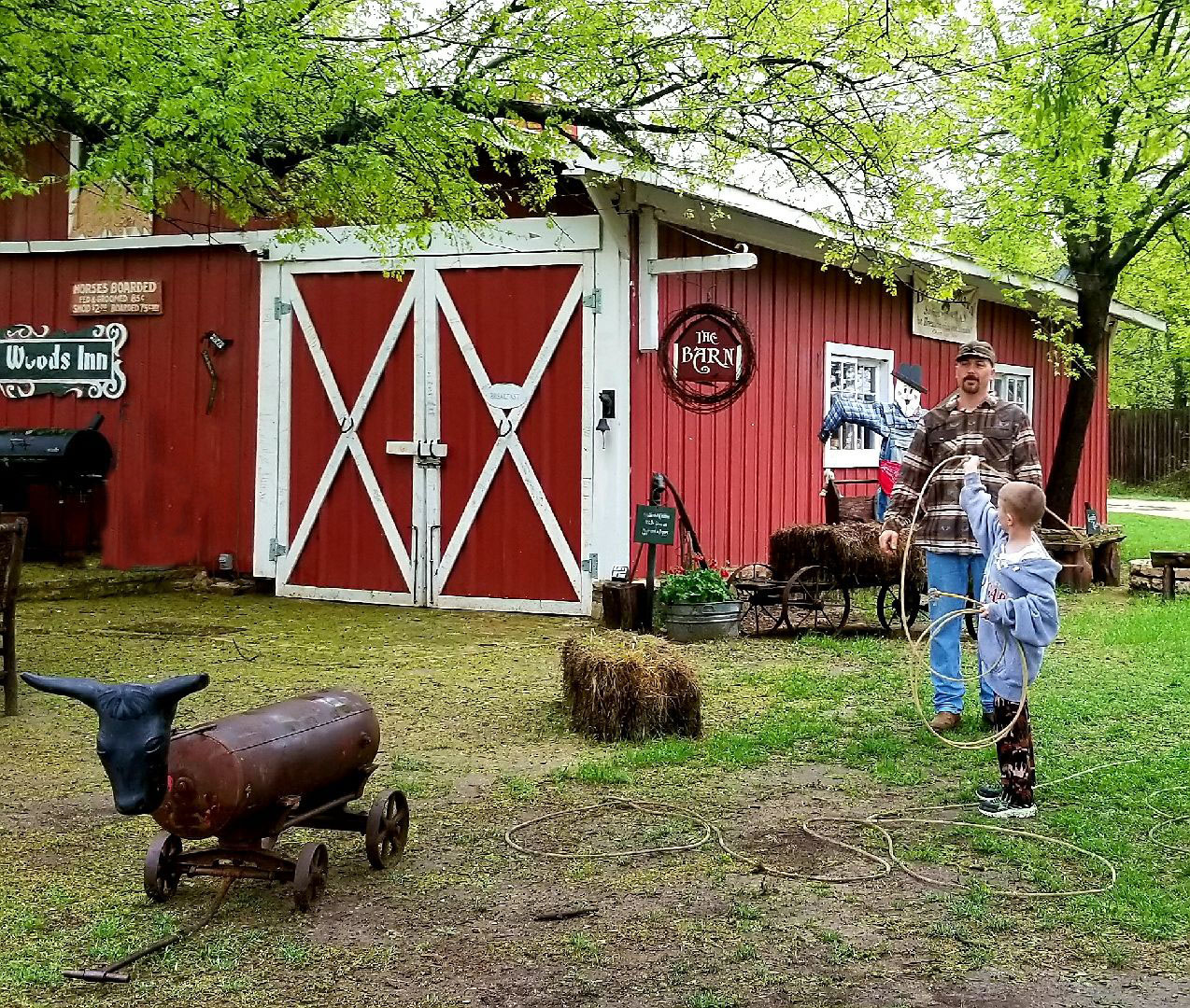 Dad and son practice roping a cow dummy in front of a barn