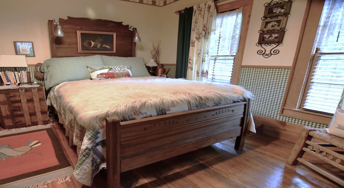 A queen size wooden frame bed with green and white check quilt and wooden floor