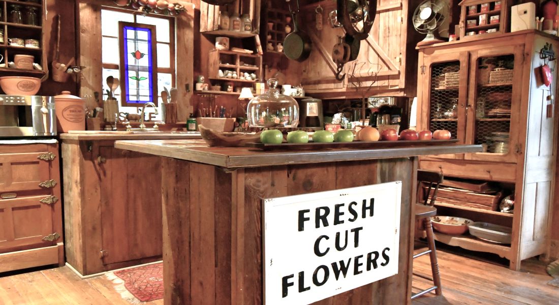 A log cabin feel with wooden island with large white sign with black letters saying Flowers For Sale, sink in background with antique white refrigerator