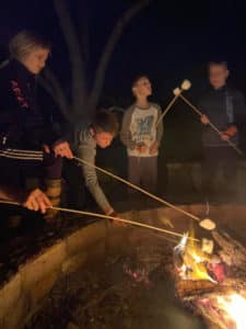 3 kids roast marshmallows over a campfire at night