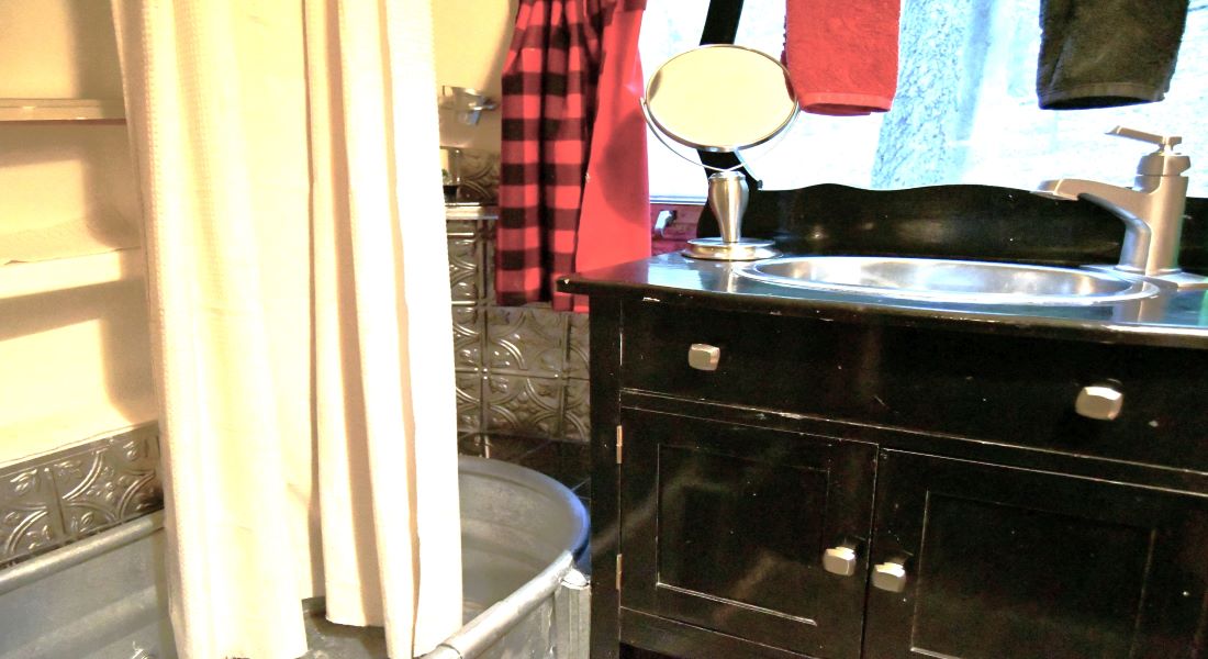 A black dresser with a sink in the top with silver mirror and a white shower on the left