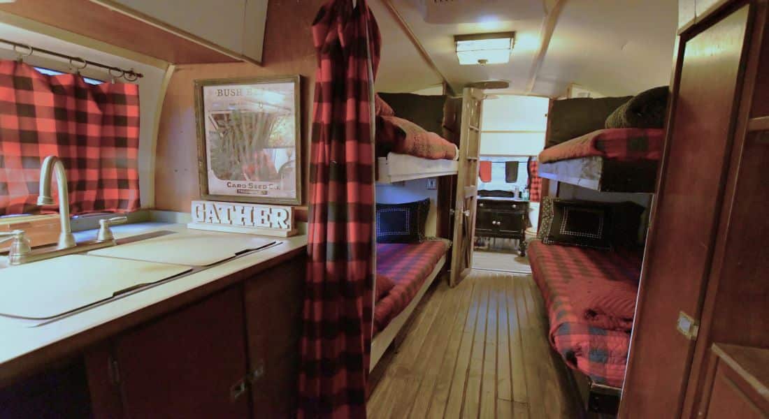 A silver double sink on the left with a long shot of 2 sets of twin bunk beds on each side with red and black check quilts