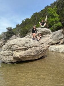 3 kids stand on large boulders by the Paluxy River