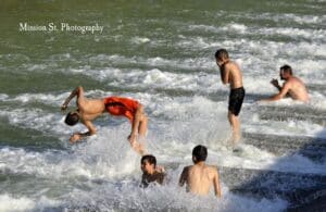 Teenagers jump and swim in the Paluxy River off of a cement spillway