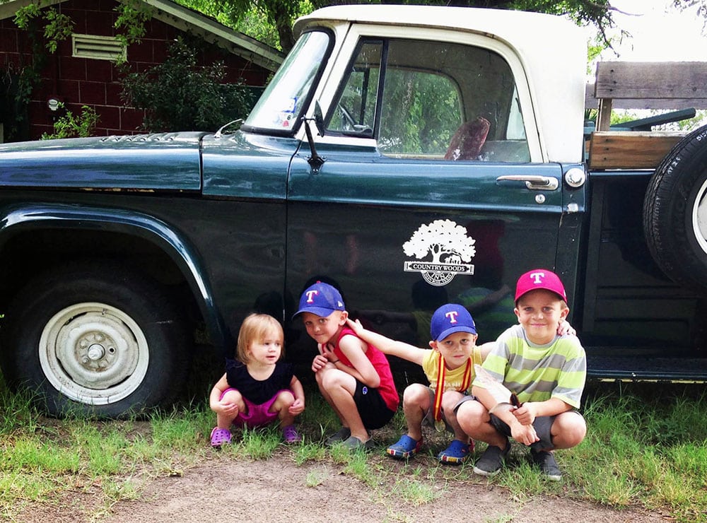 4 Kids kneel in front of an old green and white Dodge pickup