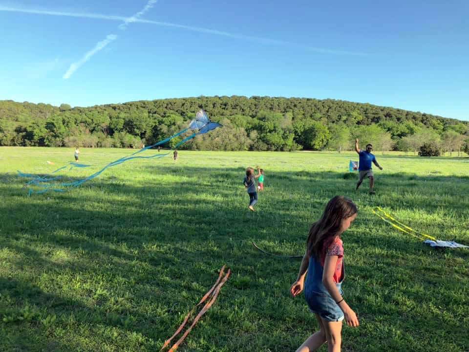 Kids with colorful kites run through a green meadow