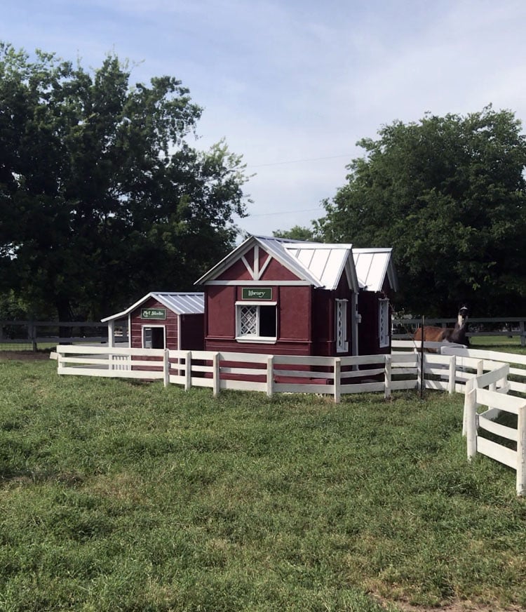 A small kid's library and kid's art studio look like small barns in the middle of a corral with a white fence