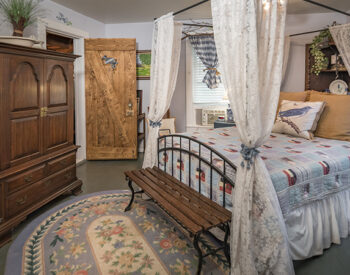 A blue themed queen bed with white lace canopy with wood floors and walls