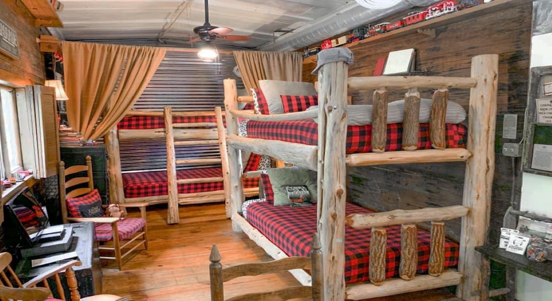 Two sets of twin bunkbeds with log cabin sides and black and red check bedspreads with stripe pillows on them
