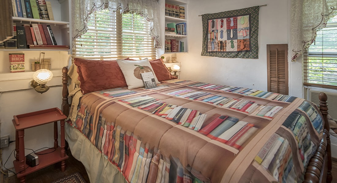 A full size bed with quilt showing books and bookshelf behind with