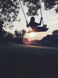 A silhouette of a young girl swinging as the sun goes down in front of her 