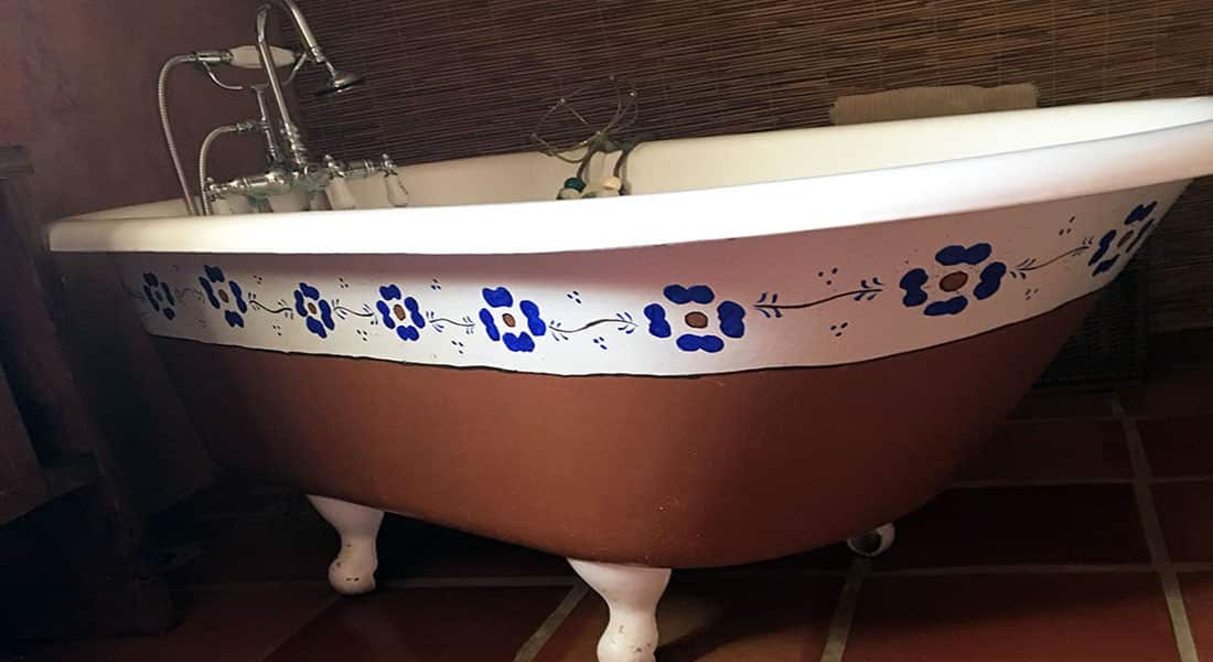 A hand painted claw foot tub with white trim and blue flowers sits in the loft bathroom.