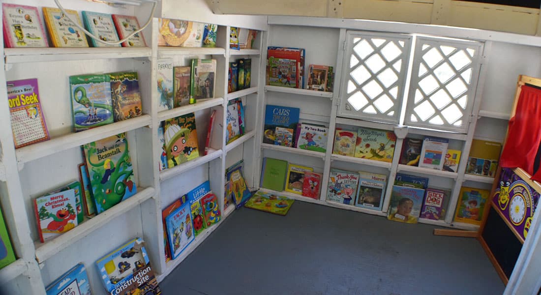 Children's books on white shelves inside a kid's library playhouse