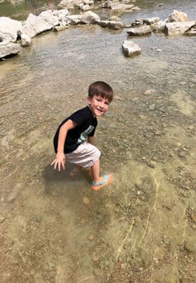 A young boy bends down to feel the dinosaur tracks in the river bed.