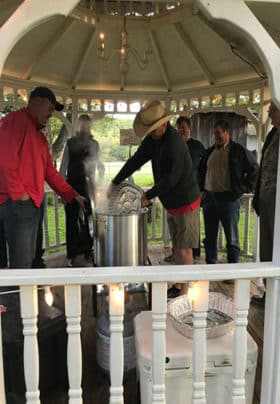 A group of men stand in a gazebo pouring shrimp into a cooker for a shrimp boil.