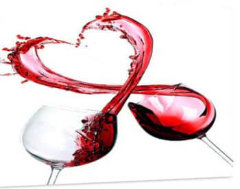 Two clear wine glasses clink together with red wine spilling out into a heart shape