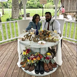 Groom in white next to a bride in blue sitting at a round table in a gazebo