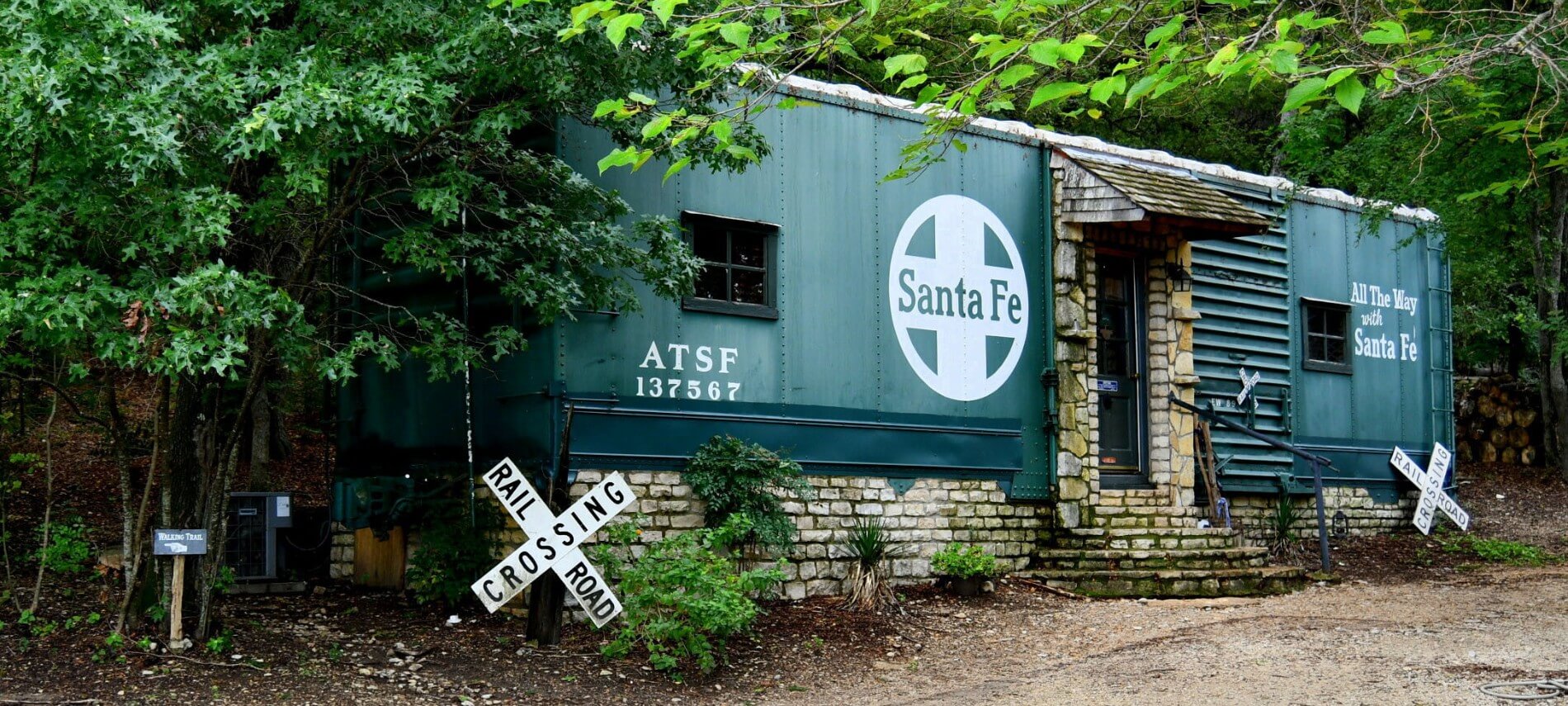 An old green Santa Fe railroad car on a stone foundation with a small stone porch leading to a door.