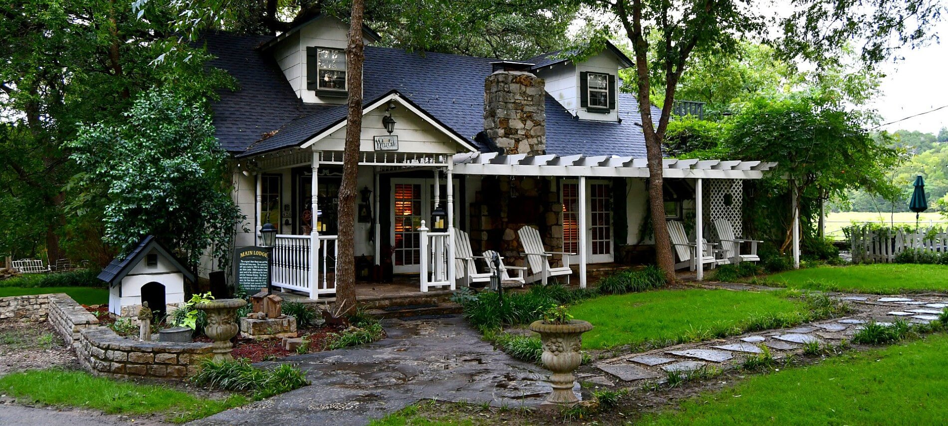 Pretty cabin with a black roof fronted by a stone path and green lawn.