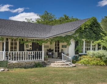 White cabin with green ivy growing over it and a stone porch.