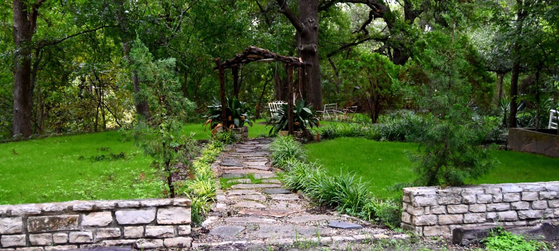 Stone wall and path leading to a wooden swing in a green area.