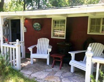 Two white adirondack chairs on the porch of a red cabin.