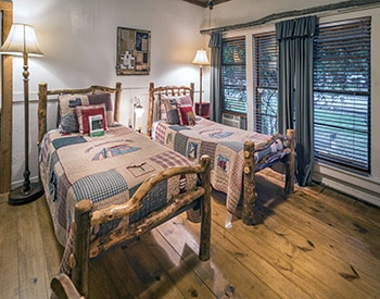 Twin log beds made up with quilts in a bedroom with white walls.