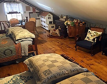 Cozy bedroom under eaves with two twin beds, a doll house and child-sized furniture.