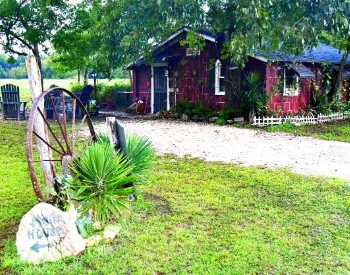 Red cabin surrounded by green trees with a seating area out front.