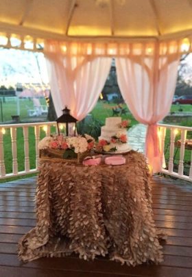 Table decorated for a wedding with a white wedding cake in a gazebo.