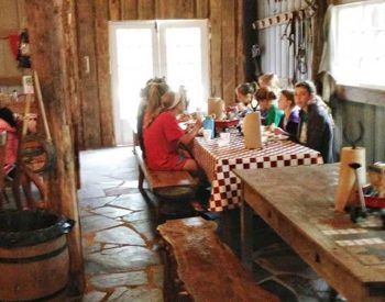 A rustic dinign area with checked tablecoths and barrels holds two groups of people.