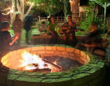 A group of people around a firepit, singing and playing the guitar.