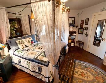 Homey bedroom with a bed canopied in lace covered with a quilt and a painted bedside table.